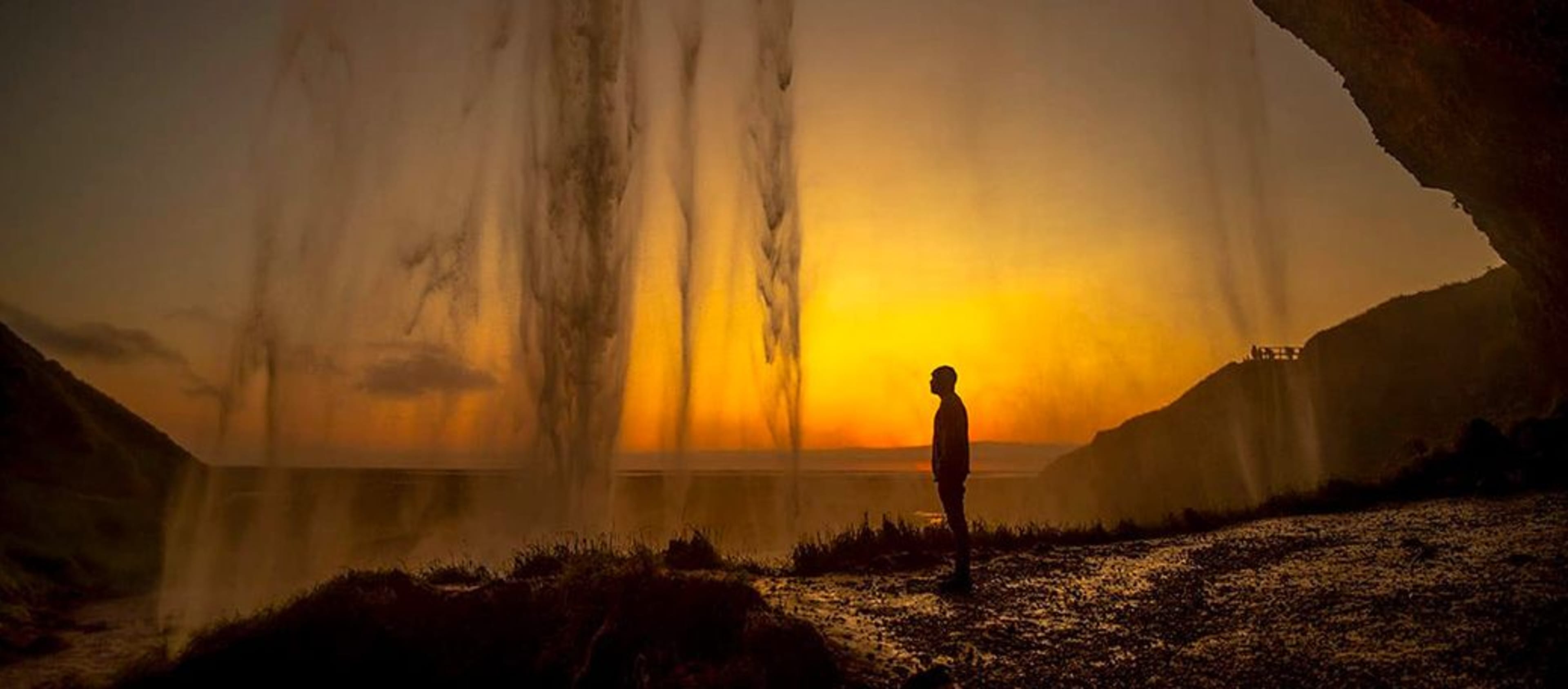 man standing at seljalandsfoss in sunset